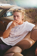 Coastal Club Tee worn on model at the beach, sun-faded cream cotton